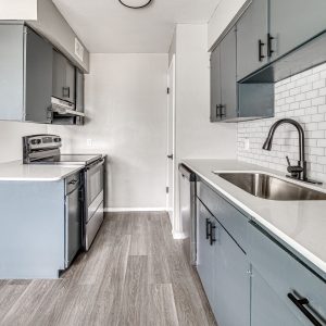 Galley kitchen with gray cabinets, stainless appliances, subway tile backsplash, and quartz countertops