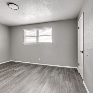 Empty bedroom with gray walls, wood-look flooring, a window with blinds, and a closet door.
