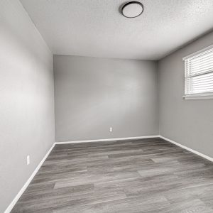 Empty bedroom with gray walls, wood-look flooring, and a window with white blinds