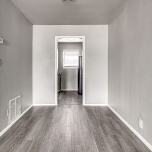 Empty hallway with wood-look flooring leading to a kitchen with window blinds