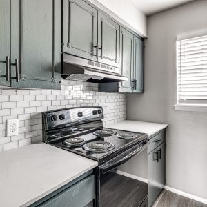 Kitchen with sage green cabinets, subway tile backsplash, black stove, and white countertops