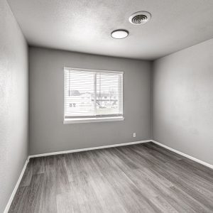 Empty room with gray walls, wood-look flooring, and a window with blinds overlooking a neighborhood