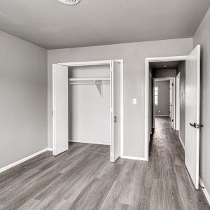Empty bedroom with open bi-fold closet door and hallway view, gray walls and wood-style flooring