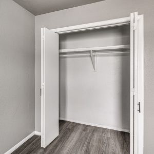 Open bifold closet door revealing empty shelf and hanging rod above wood-look flooring