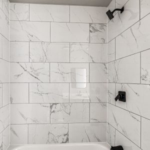 Shower corner with white marble-look tile, black fixtures, and a rainfall showerhead