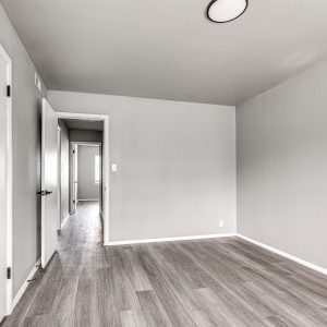 Empty bedroom with wood-look flooring, gray walls, and an open closet door leading to a hallway