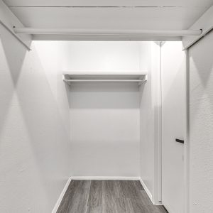 Empty closet with white shelving and hanging rods above a gray wood-look floor.