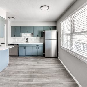 Kitchen with blue cabinets, stainless steel appliances, subway tile backsplash, and large windows